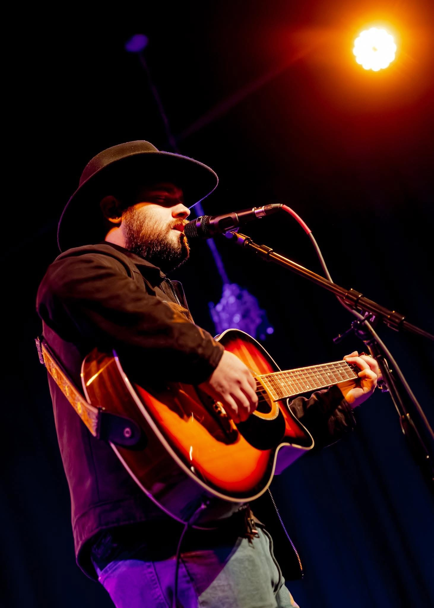 Jon singing and playing acoustic guitar under warm stage lights.